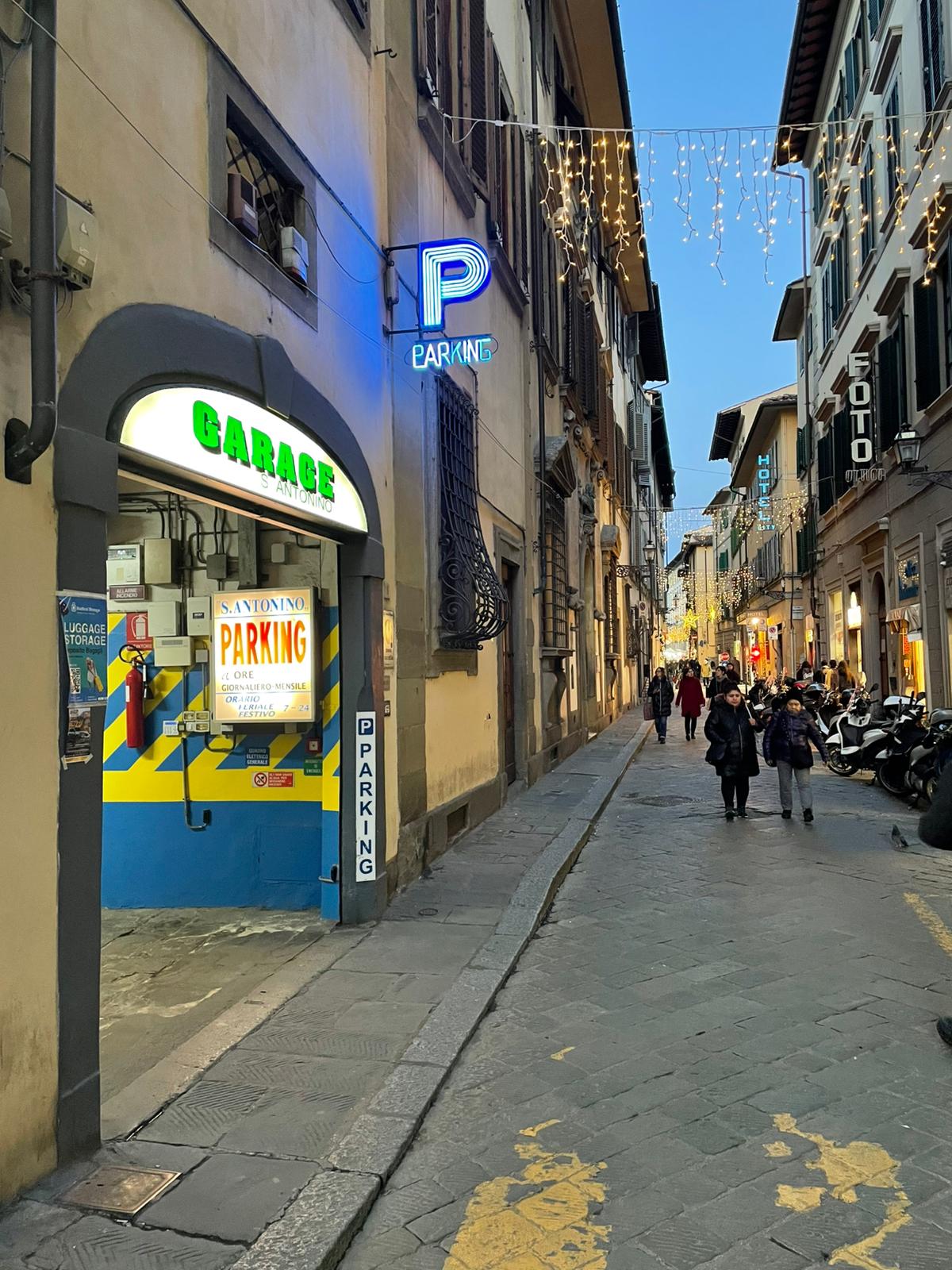 Street view of Garage S. Antonino on Via Sant'Antonino with neon P 'Parking' sign and lit GARAGE entrance, Florence