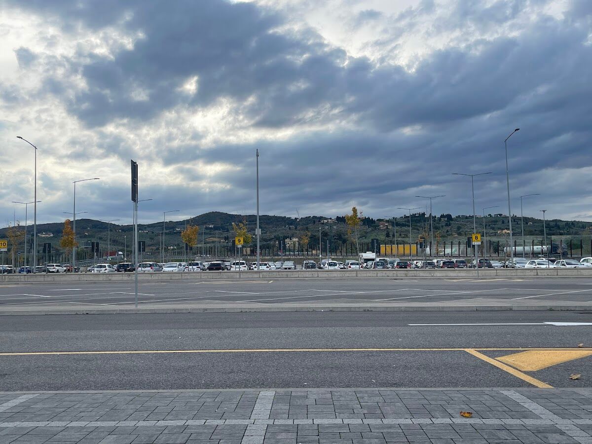 Park & Ride Villa Costanza: rows of parked cars in the open-air lot with numbered zone signs and Tuscan hills behind